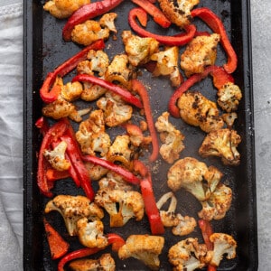 Overhead view of roasted cauliflower and red bell pepper strips on a baking sheet