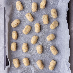 A batch of unbaked cauliflower tots spread out on a parchment-lined baking sheet