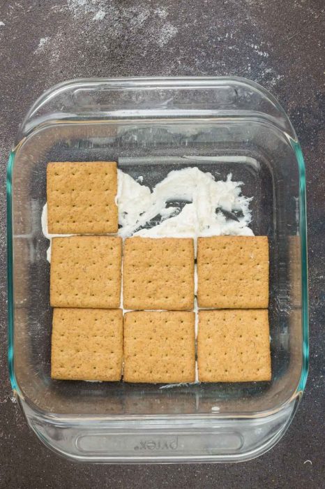 Graham crackers layered over cheesecake filling in a square baking dish