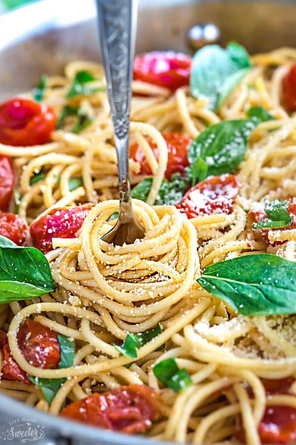 Close up of a fork twirling spaghetti in a pot of cherry tomato pasta, topped with basil leaves and parmesan cheese.
