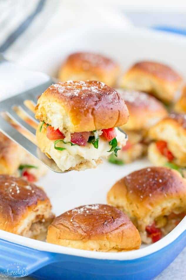 Chicken bruschetta sliders in a baking dish with one on a serving spatula