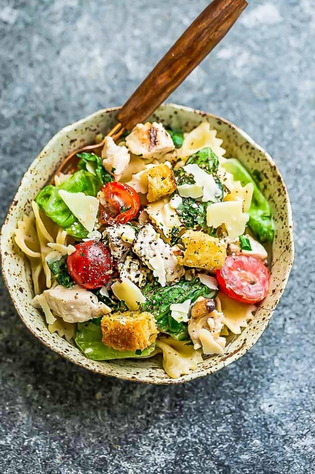 Chicken Caesar pasta salad in beige speckled bowl on grey surface.