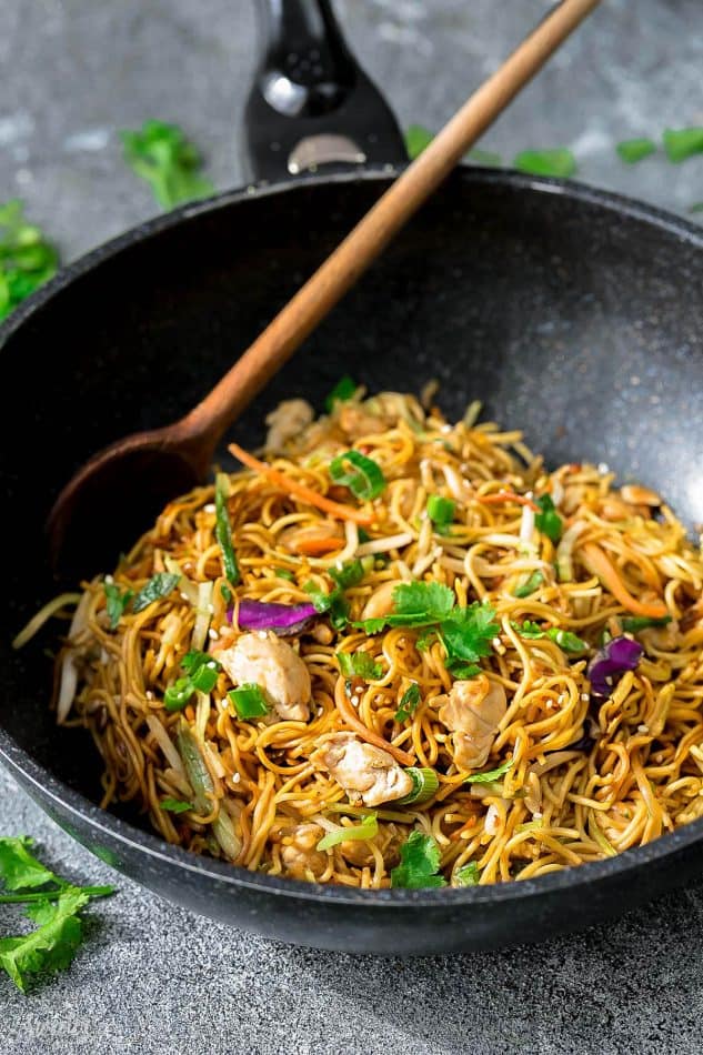 Side view of Chicken Chow Mein in a wok with a wooden spoon