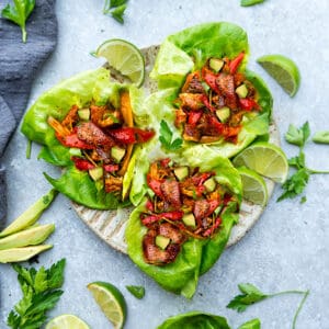 Top view of chicken fajita wraps in lettuce on a beige plate on grey background