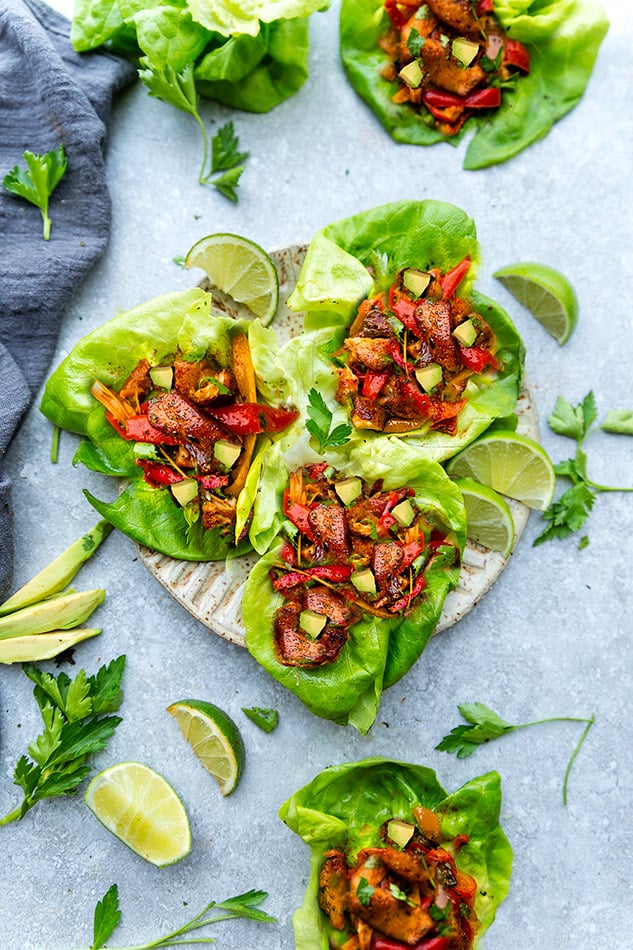 Top view of chicken fajita wraps in lettuce on a beige plate on grey background