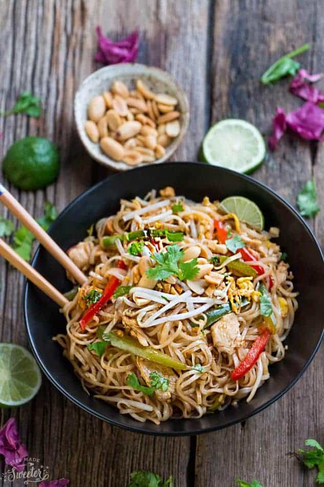 Gluten free Chicken Pad Thai recipe in a large black serving bowl with brown chopsticks on a wooden table.