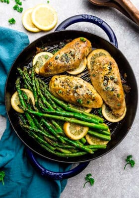 Top view of Easy Chicken Piccata with asparagus and capers in a blue cast iron pan on a grey background