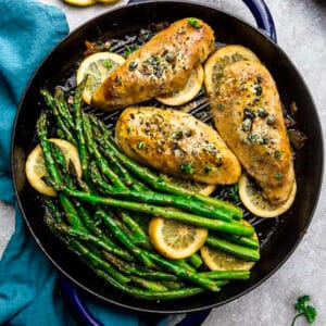 Top view of Easy Chicken Piccata with asparagus and capers in a blue cast iron pan on a grey background