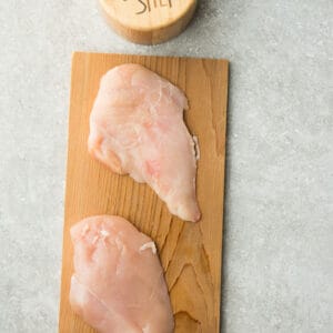 Two Raw Chicken Breasts on a Cutting Board Beside a Salt Shaker