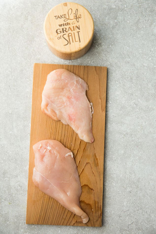 Two Raw Chicken Breasts on a Cutting Board Beside a Salt Shaker