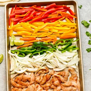 Thinly sliced vegetables and chicken on a metal baking sheet with a raised rim
