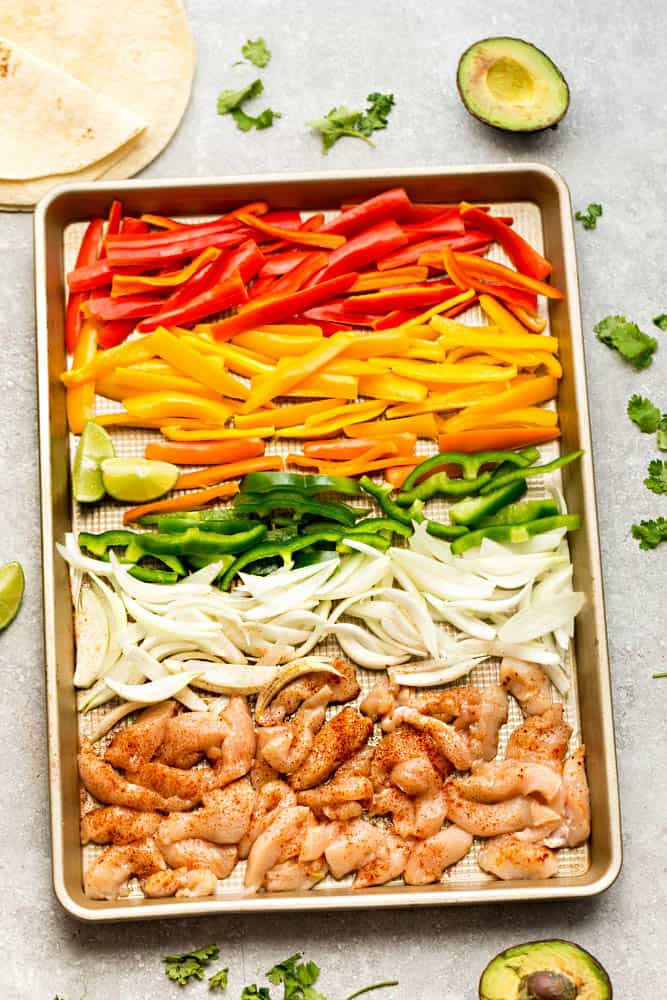 Thinly sliced vegetables and chicken on a metal baking sheet with a raised rim