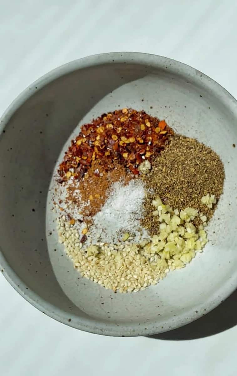 Garlic, spices and chili powder in a white bowl.