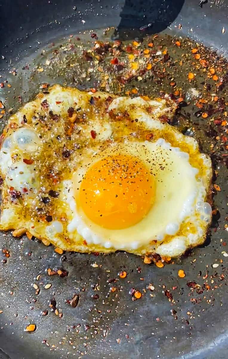One fried egg in a hot pan with chili crunch oil.