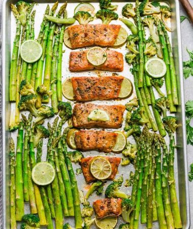 Top view of a sheet pan with Chili Lime Salmon fillets with asparagus and broccoli and lime slices