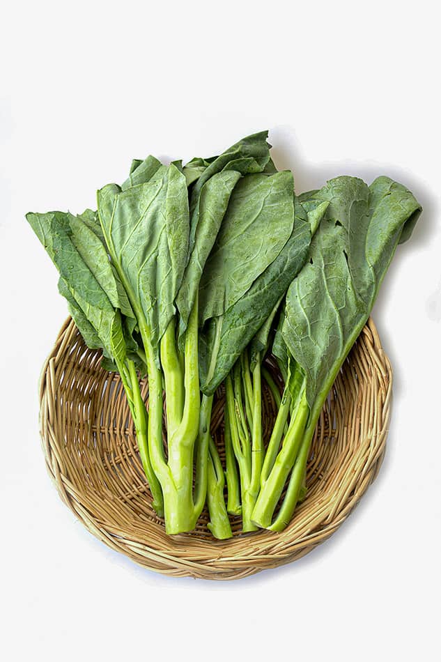 Fresh Chinese broccoli (gai lan) in an oval basket on a white background