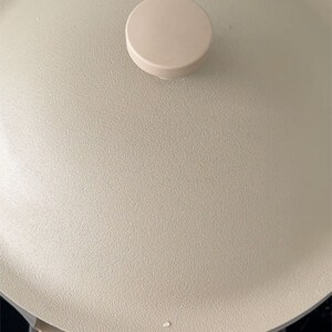 A beige frying pan over a burner with the lid