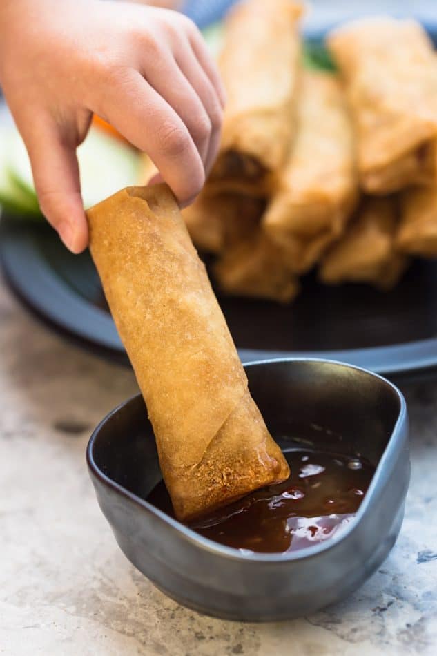 A crispy Chinese spring roll being dipped into a small dish of sauce