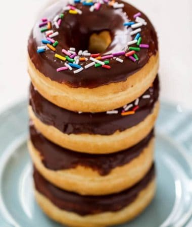 A stack of Chocolate Frosted Donuts with Sprinkles on a plate