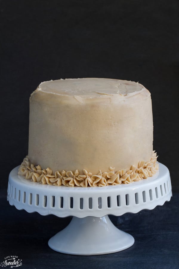 Side view of an entire snickers cake with buttercream frosting on a white cake stand.