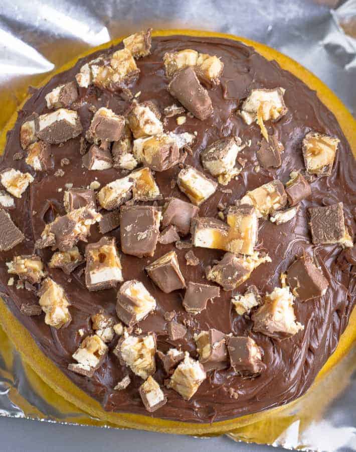 Close-up of a layer of snickers cake with melted chocolate and chopped Snickers.