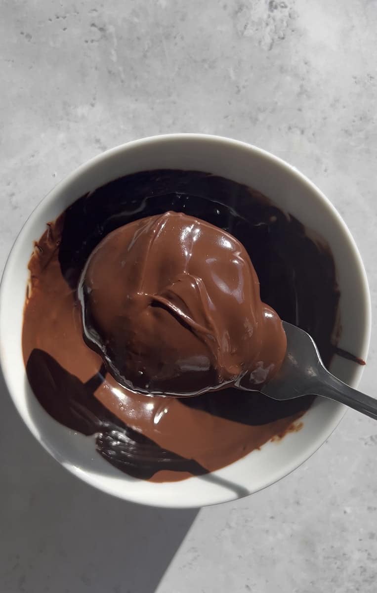 A fork dipping a strawberry jam bite into a bowl of melted chocolate