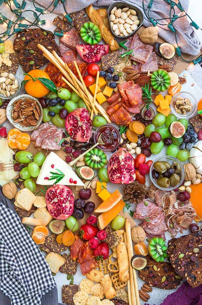Top view of a holiday cheese board with a variety of crackers, nuts, fruits, meats, and cheeses