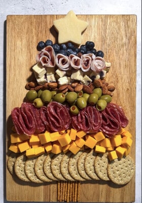 Assorted crackers, cheese, fruit and nuts shaped into a christmas tree on a wooden cutting board