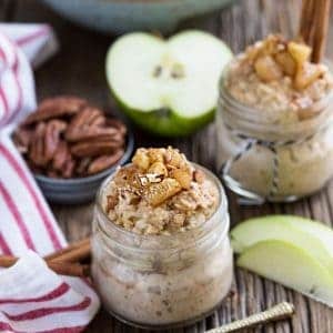Two jars of Cinnamon Apple Pie Overnight Oats next to a bowl of pecans, apple slices, and utensils