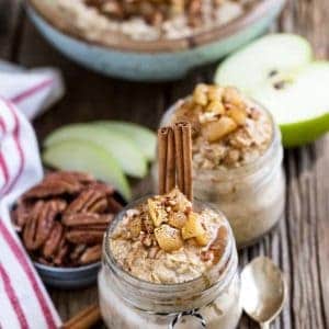 Two jars of Cinnamon Apple Pie Overnight Oats next to a bowl of pecans, apple slices, and utensils