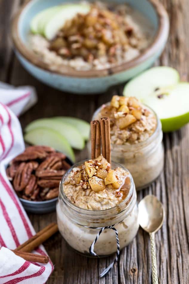 Two jars of Cinnamon Apple Pie Overnight Oats with cinnamon sticks, pecans, and apple slices