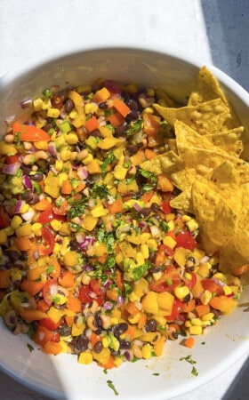 Black bean and corn salad in a large white mixing bowl with tortilla chips