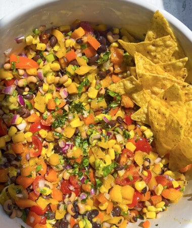 Black bean and corn salad in a large white mixing bowl with tortilla chips