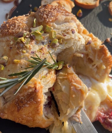Puffed pastry wrapped around baked brie on a baking sheet