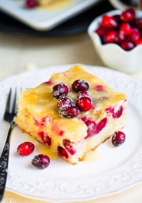 A slice of cranberry Christmas cake topped with a buttery sauce on a white plate with a fork.