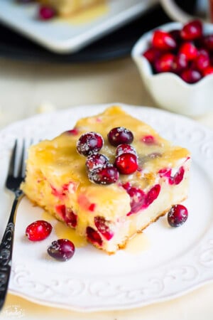 A slice of cranberry Christmas cake topped with a buttery sauce on a white plate with a fork.