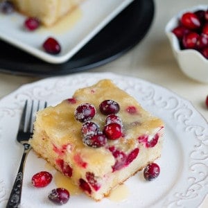 A slice of cranberry Christmas cake topped with a buttery sauce on a white plate with a fork.