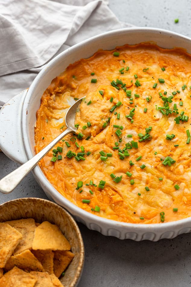 45 degree shot of a batch of vegan buffalo chicken dip in a white round baking dish with a spoon