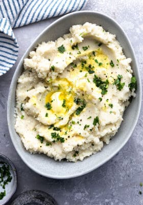 Top view of creamy cauliflower mash in a grey bowl on a wooden cutting board
