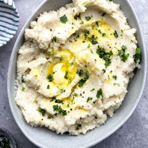 Top view of creamy cauliflower mash in a grey bowl on a wooden cutting board