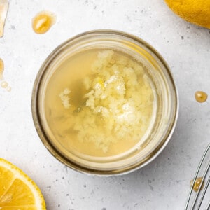 Top view of ingredients to make lemon tahini dressing (lemon juice, tahini, garlic and maple syrup) in a glass jar