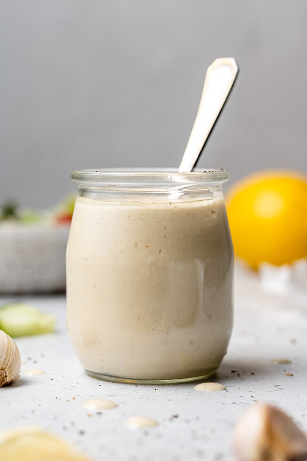 Side view of lemon tahinin dressing in a small jar with a spoon