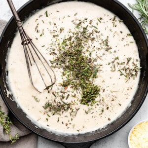Overhead view of cream sauce with herbs in a skillet with a whisk