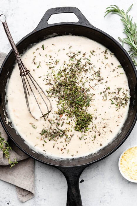 Overhead view of cream sauce with herbs in a skillet with a whisk