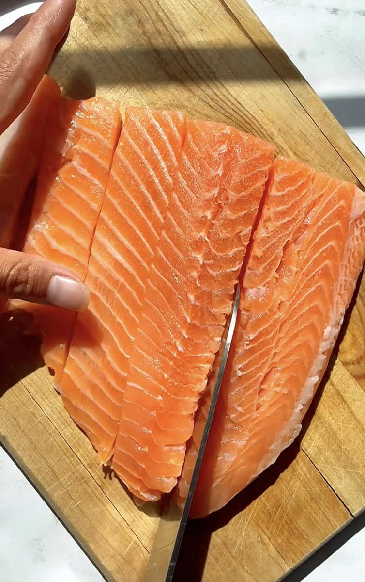 A raw salmon filet on a wooden cutting board with a knife