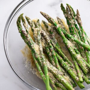 Fresh asparagus stalks with seasonings in a clear mixing bowl
