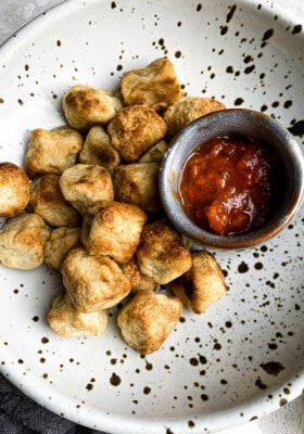 Close-up view of crispy air fried cauliflower gnocchi in a white speckled bowl with a side of marinara sauce