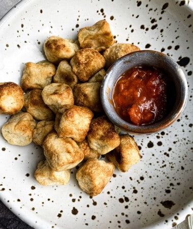 Close-up view of crispy air fried cauliflower gnocchi in a white speckled bowl with a side of marinara sauce
