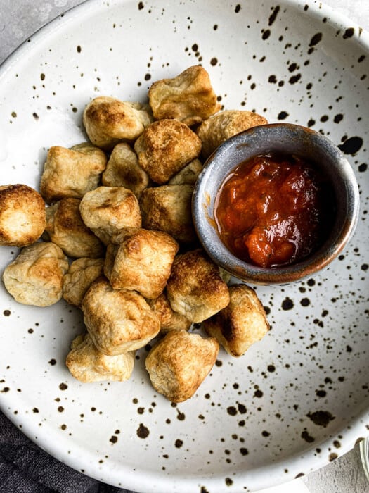 Close-up view of crispy air fried cauliflower gnocchi in a white speckled bowl with a side of marinara sauce