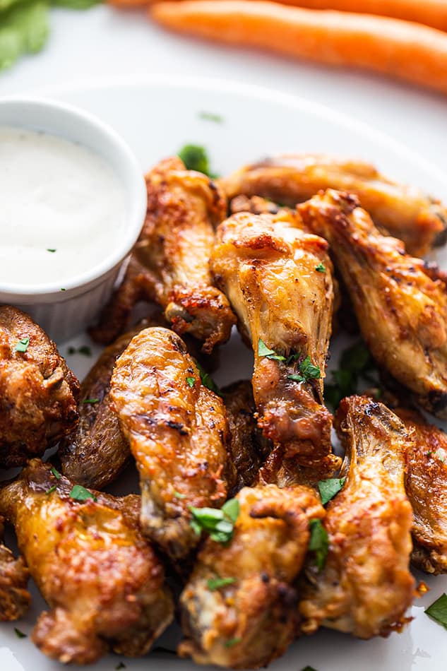 Close-up of crispy Air Fryer Chicken Wings on a plate next to a cup of creamy dipping sauce